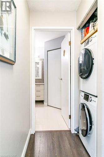 Dedicated laundry area featuring stacked front-load washer and dryer units with a built-in wood shelf - 175 Hunter Street E Unit# 103, Hamilton, ON - Indoor Photo Showing Laundry Room
