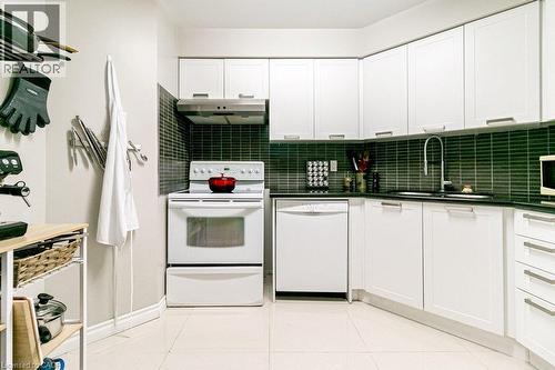 Modern kitchen featuring white cabinetry with brushed nickel hardware, a dark tile backsplash, and dark countertops - 175 Hunter Street E Unit# 103, Hamilton, ON - Indoor Photo Showing Kitchen
