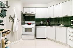 Modern kitchen featuring white cabinetry with brushed nickel hardware, a dark tile backsplash, and dark countertops - 