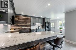 Modern kitchen featuring a large island with a light-toned countertop, gray cabinetry, a wood-finish accent wall, and recessed lighting - 