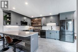 Modern kitchen featuring gray shaker cabinetry, stainless steel appliances, a white subway tile backsplash, a large island with a light-toned countertop, and wood-panel accents - 