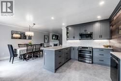 Open-concept kitchen featuring gray cabinetry, stainless steel appliances, a subway tile backsplash, and light-toned countertops - 