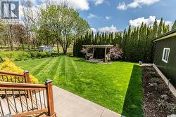 Expansive lawn with striped mowing pattern, bordered by mature trees and evergreen privacy hedging - 