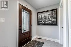 Front entry featuring a dark wood-finish door with decorative glass inserts, white trim, light gray walls, and light gray flooring - 