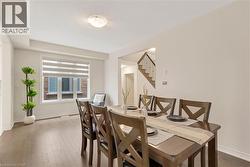 Spacious dining area featuring wood-finish flooring, a large window with horizontal blinds, and a staircase with wood railings - 