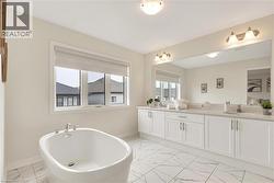 Contemporary bathroom featuring a freestanding soaking tub with chrome fixtures, a broad window, and elegant white cabinetry with a light-toned countertop - 