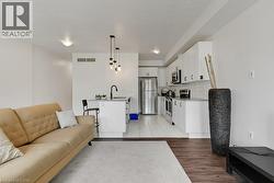 Open-concept living space featuring wood-finish flooring, a kitchen island with seating, a white subway tile backsplash, white cabinetry, and stainless steel appliances - 