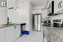 Modern kitchen featuring white cabinetry, granite-finish countertops, stainless steel appliances, and white tile flooring - 