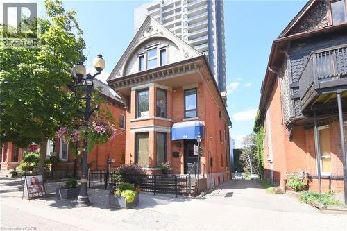 Brick exterior with a prominent bay window, arched gable dormer, and a blue awning - 108 George Street, Hamilton, ON 