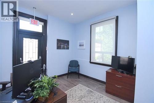 Entryway featuring a dark wood door with decorative glass, wood-finish flooring, light blue walls, and a large window with a roller shade - 108 George Street, Hamilton, ON 
