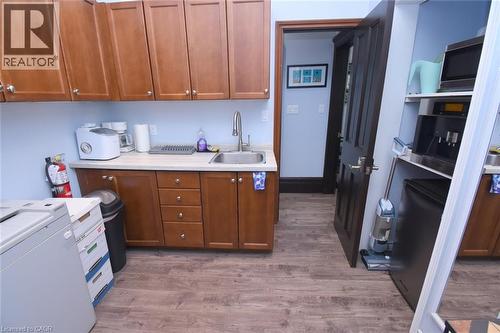 Functional kitchen area featuring wood-finish flooring, light blue walls, and amber-toned cabinetry with silver hardware - 108 George Street, Hamilton, ON 