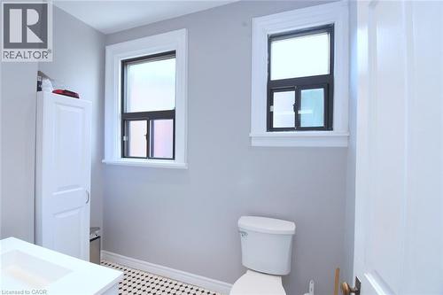 Bathroom featuring a white vanity with an integrated sink, black and white mosaic tile flooring, and two windows with white trim - 108 George Street, Hamilton, ON 