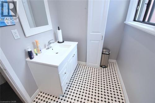 Bathroom featuring a white vanity with integrated sink, chrome faucet, white framed mirror, and a white storage cabinet - 108 George Street, Hamilton, ON 
