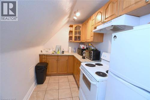 Compact kitchen featuring wood cabinetry, solid surface countertops, a white electric range, and a white refrigerator - 108 George Street, Hamilton, ON 