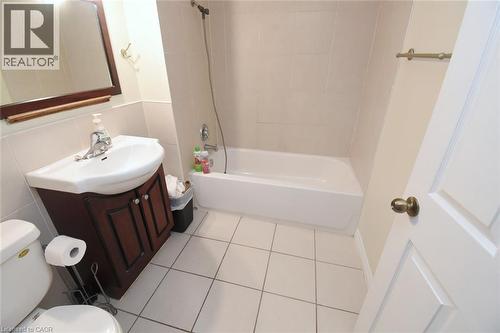 Full bathroom featuring a white tub, ceramic wall tiles, and a vanity with a white basin and wood-finish cabinetry - 108 George Street, Hamilton, ON 