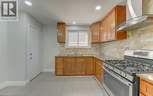 Kitchen featuring light wood cabinetry, stone-look tile backsplash, stainless steel gas range, stainless steel range hood, and light gray tile flooring - 80 Lower Canada Crescent, Kitchener, ON - Indoor Photo Showing Kitchen