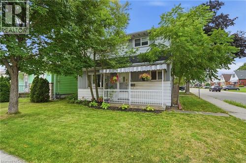 Two-story residence featuring a covered front porch with striped awning, front yard with mature trees and established landscaping, and a paved sidewalk - 432 Upper Sherman Avenue, Hamilton, ON - Outdoor