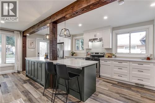 Modern kitchen featuring exposed wood beams, wood-finish flooring, white cabinetry, a contrasting island with seating, and stainless steel appliances - 323 Cranbrook Drive, Hamilton, ON - Indoor Photo Showing Kitchen With Upgraded Kitchen