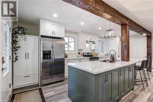 Open-concept kitchen featuring a central island with a white countertop and seating, stainless steel appliances, white cabinetry, rustic wood beams, and wood-finish flooring - 323 Cranbrook Drive, Hamilton, ON - Indoor Photo Showing Kitchen With Upgraded Kitchen