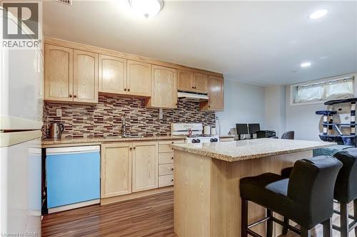 Kitchen area featuring wood-finish flooring, light wood cabinetry, a mosaic tile backsplash, and a breakfast bar with a stone-finish countertop - 323 Cranbrook Drive, Hamilton, ON - Indoor Photo Showing Kitchen