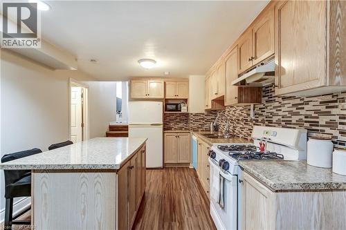 Kitchen featuring wood-finish flooring, light wood cabinetry, stone countertops, a tiled backsplash, and a central island - 323 Cranbrook Drive, Hamilton, ON - Indoor Photo Showing Kitchen With Upgraded Kitchen