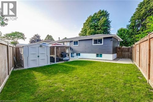 Expansive backyard featuring a manicured lawn, full privacy fencing, and a concrete patio area - 323 Cranbrook Drive, Hamilton, ON - Outdoor With Exterior