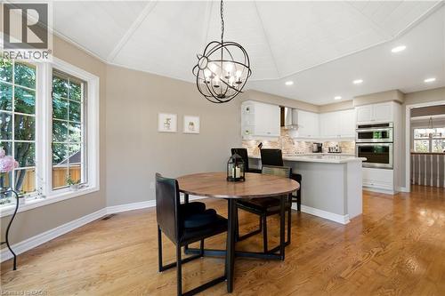 Open-concept kitchen featuring white cabinetry, stainless steel double wall ovens, a center island with bar seating, and a stone-finish backsplash - 1090 Crofton Way, Burlington, ON - Indoor Photo Showing Dining Room