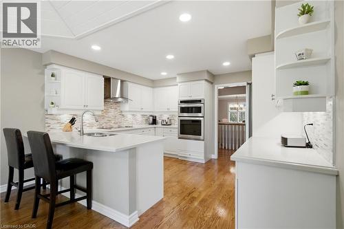 Bright kitchen featuring white cabinetry, integrated stainless steel appliances, a multi-tone tile backsplash, and wood-finish flooring - 1090 Crofton Way, Burlington, ON - Indoor Photo Showing Kitchen With Upgraded Kitchen