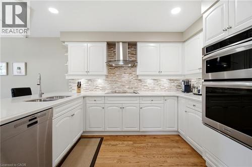 Bright kitchen featuring white cabinetry, light-toned countertops, stainless steel appliances, wood-finish flooring, and a textured tile backsplash - 1090 Crofton Way, Burlington, ON - Indoor Photo Showing Kitchen With Double Sink With Upgraded Kitchen