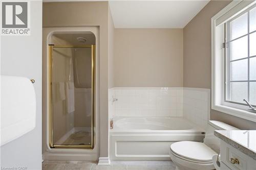 Bathroom featuring a shower stall with brass-toned frame, a built-in bathtub with white tile surround, a window with grid pattern, and a vanity with a light-colored countertop - 1090 Crofton Way, Burlington, ON - Indoor Photo Showing Bathroom