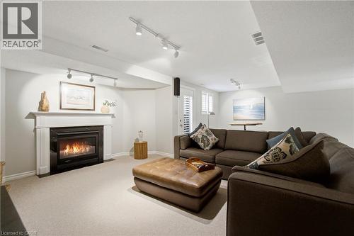 Built-in fireplace with white mantel and black surround, track lighting fixtures, light-toned carpet flooring, white walls, and white plantation shutters - 1090 Crofton Way, Burlington, ON - Indoor Photo Showing Living Room With Fireplace