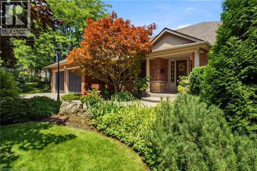 Brick exterior with a covered porch entry, surrounded by mature landscaping and a paved driveway - 1090 Crofton Way, Burlington, ON - Outdoor
