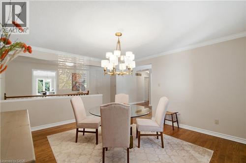 Dining area featuring a brass chandelier, crown molding, wood-finish flooring, and a half-wall partition with a wood railing - 1090 Crofton Way, Burlington, ON - Indoor Photo Showing Dining Room