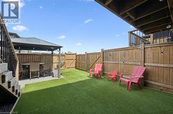 Private backyard featuring artificial turf, a wood privacy fence, and a covered patio area with string lighting - 