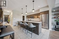 Modern kitchen featuring a large center island with seating, stainless steel appliances, dark wood-finish cabinetry, white subway tile backsplash, and recessed lighting - 