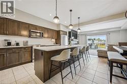 Open-concept kitchen and dining area featuring a spacious island with seating, dark wood-finish cabinetry, stainless steel appliances, white subway tile backsplash, and light tile flooring - 