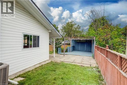 Rear exterior featuring white horizontal siding, a framed window, concrete patio, grassed area, and a red-stained wooden fence - 182 Avalon Place, Kitchener, ON - Outdoor With Exterior