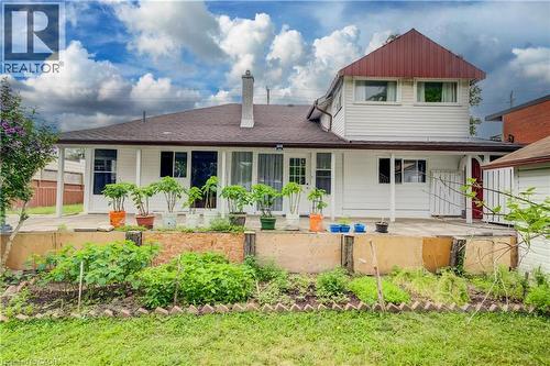 Rear exterior featuring white horizontal siding, a two-story addition with a red metal roof, a ground-level patio, a fenced backyard, and a garden area - 182 Avalon Place, Kitchener, ON - Outdoor
