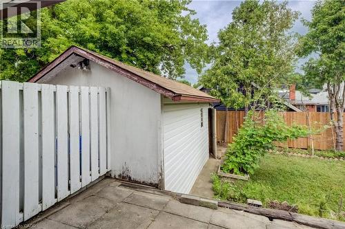 Detached storage structure featuring white siding and a shingled roof, accompanied by a white picket fence and a concrete patio - 182 Avalon Place, Kitchener, ON - Outdoor