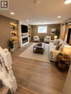 Spacious living area featuring wood-finish flooring, recessed lighting, and a modern fireplace with a white tile surround - 