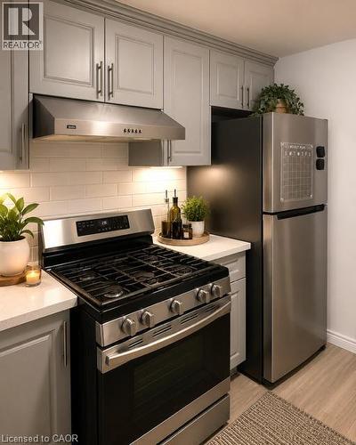 Kitchen featuring light grey cabinetry, a stainless steel range with overhead ventilation, a stainless steel refrigerator, white subway tile backsplash, and light wood-finish flooring - 143 Grenfell Place, London, ON - Indoor Photo Showing Kitchen