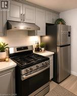 Kitchen featuring light grey cabinetry, a stainless steel range with overhead ventilation, a stainless steel refrigerator, white subway tile backsplash, and light wood-finish flooring - 