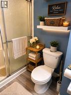 Full bathroom with wood-finish flooring, a white toilet, and a frosted glass shower enclosure - 