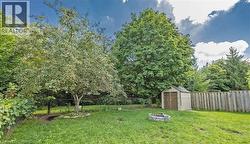 Expansive backyard featuring a manicured lawn, established trees, and a stone-lined fire pit - 