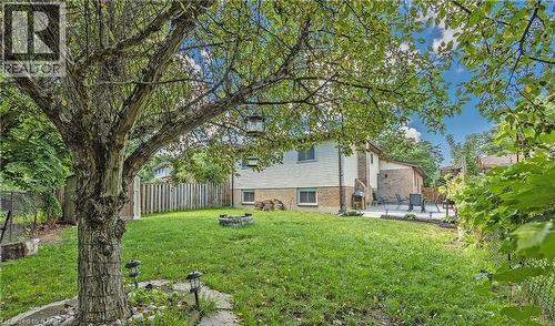 Expansive backyard featuring a mature tree, a stone-edged fire pit, a paved patio area, and perimeter fencing - 143 Grenfell Place, London, ON - Outdoor