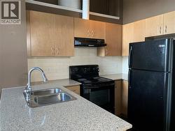 Kitchen featuring a double basin stainless steel sink with pull-down sprayer faucet, speckled light-toned countertops, light wood-finish cabinetry, white subway tile backsplash, and black appliances - 