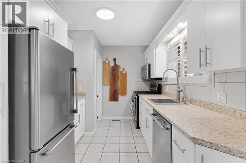 Galley kitchen featuring stainless steel appliances, white cabinetry with silver hardware, light-toned countertops, a white tile backsplash, and tile flooring - 744 Birchwood Avenue, Cambridge, ON - Indoor Photo Showing Kitchen With Upgraded Kitchen