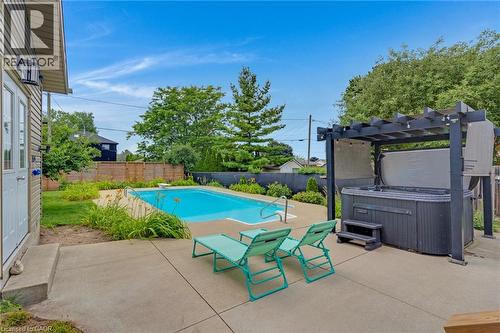Outdoor living space featuring a swimming pool, concrete patio, and a hot tub with a dark-framed pergola - 744 Birchwood Avenue, Cambridge, ON - Outdoor With In Ground Pool