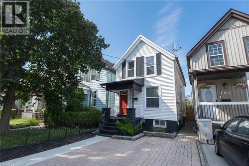 White-sided residential property featuring black window shutters and a covered porch with a red entry door - 106 Belview Avenue, Hamilton, ON - Outdoor With Facade
