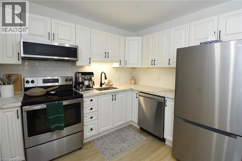 White shaker-style cabinetry with black hardware, stainless steel appliances, light-toned countertops, subway tile backsplash, and wood-finish flooring - 106 Belview Avenue, Hamilton, ON - Indoor Photo Showing Kitchen With Stainless Steel Kitchen